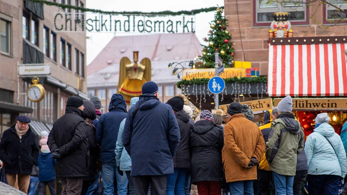 A tour group in winter coats gathered at the Christkindlesmarkt entrance by the red-and-white stalls